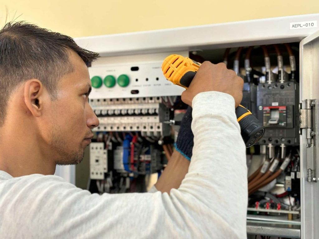 A man fixing a thermal overload relay inside an electrical box